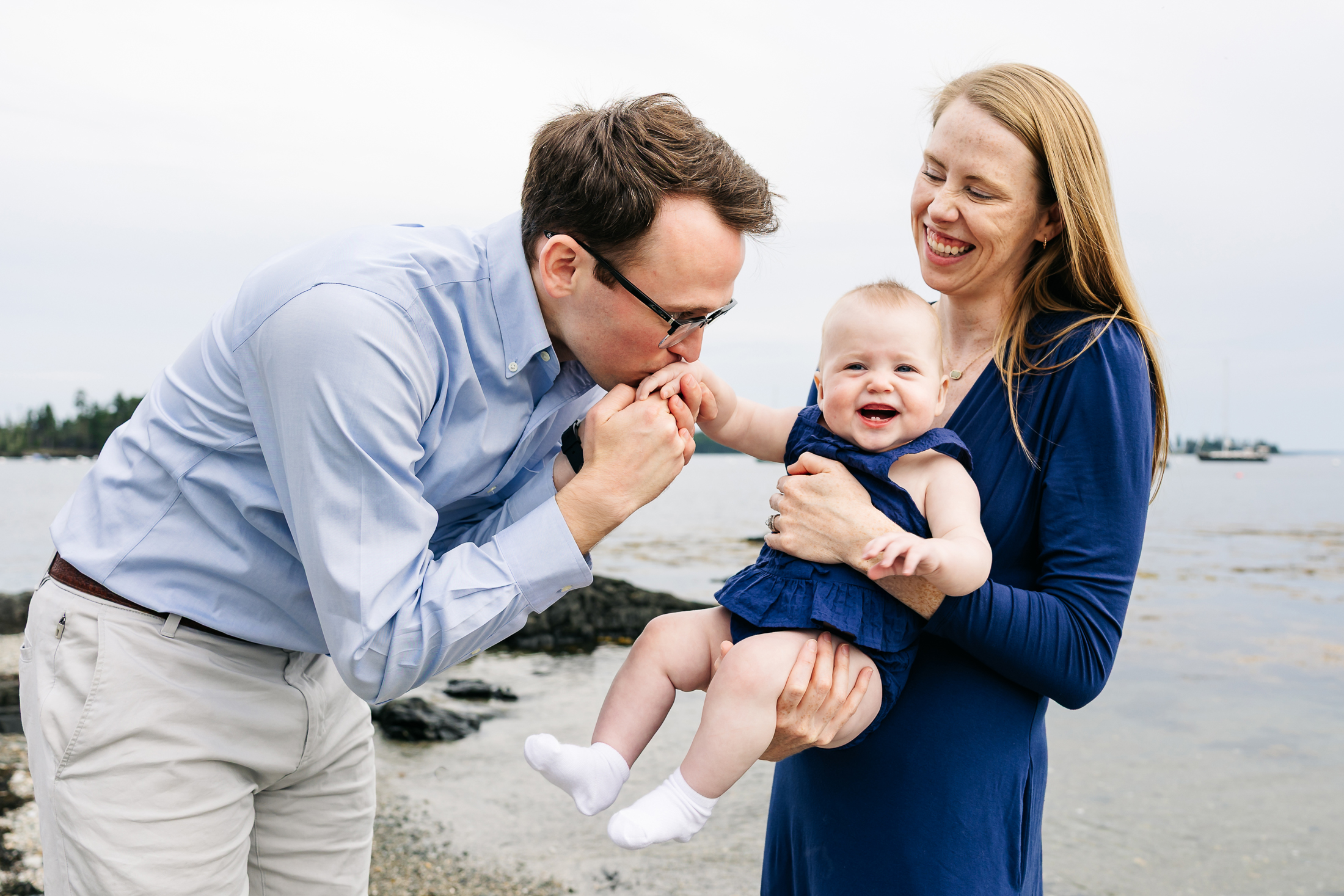 Father kisses his baby's hand while her mother holds her in Deer Isle, Maine